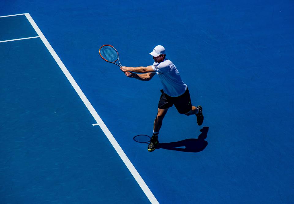 Tennisspeler die een backhand slaat op een blauwe hardcourtbaan
