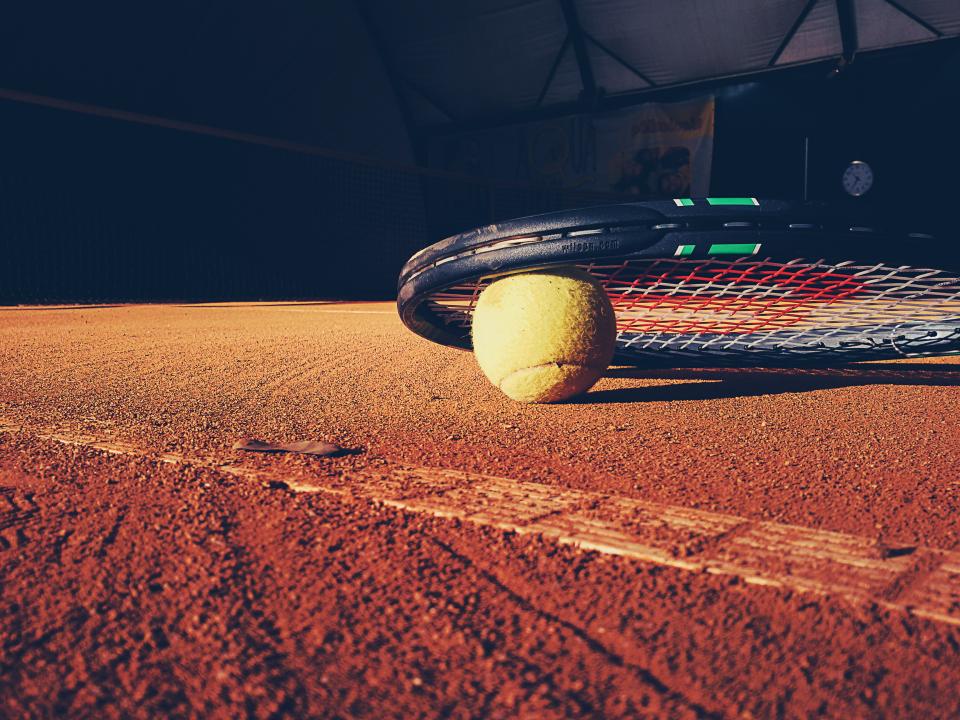 Tennisracket en bal op een gravelbaan
